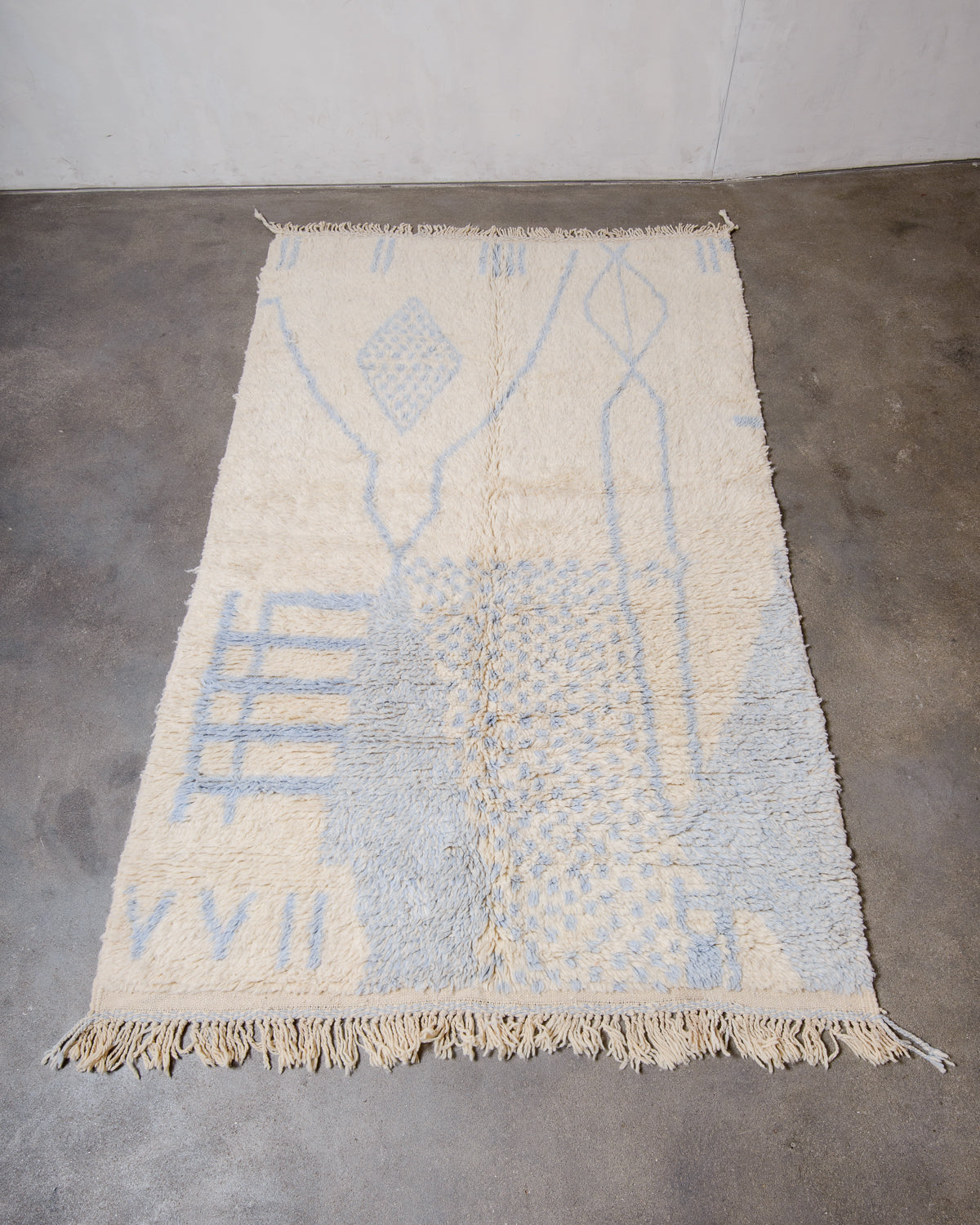 Berberlin Azilal rug in fluffy cream and light blue wool, laying flat on a concrete floor.